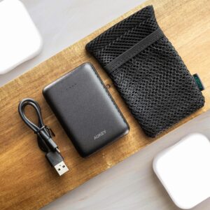 Flat lay of a black power bank with a USB cable and mesh pouch on wood.