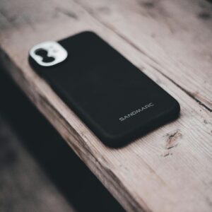 A smartphone with a Sandmarc case rests on a rustic wooden table, highlighting modern technology in a natural setting.